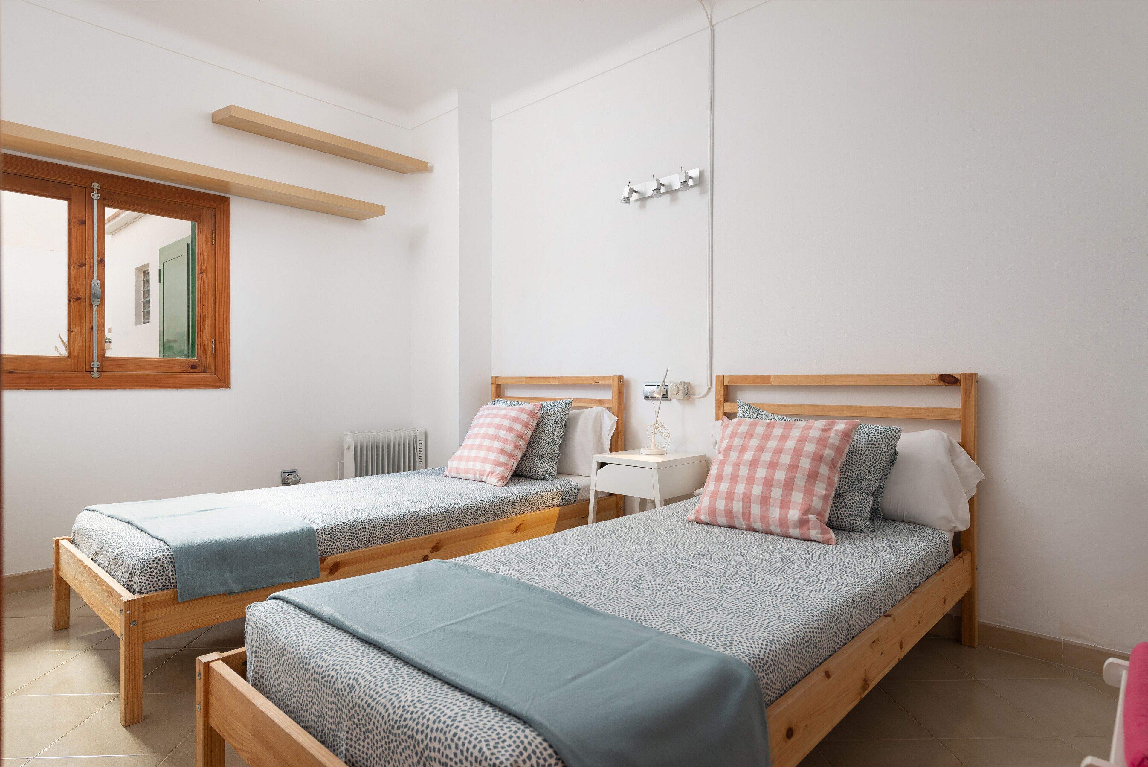 A bedroom with two wooden beds, a small bedside table, a mirror, and a window.