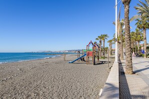A beach with a playground, palm trees, and a clear blue sky.