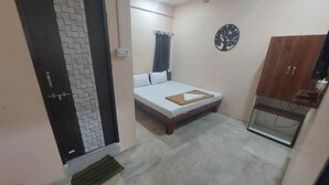 A small, well-lit room with a bed, a wardrobe, a ceiling fan, and a wall-mounted decoration. - iROOMZ City Lite Lodge (Nizamabad)