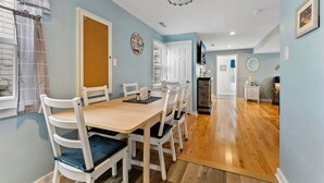 A dining area with a wooden table and white chairs, a kitchen in the background, and a blue wall.