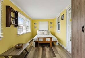 A bedroom with a bed, a wooden bench, a small table, and a wall-mounted shelf.
