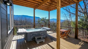 Un patio in legno con vasca idromassaggio, tavolo e sedie, con vista su un paesaggio montano.