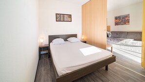 Un dormitorio moderno con una cama grande, lámparas de noche, un armario de madera y un sofá en la habitación contigua.