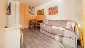 Un espacio habitable compacto con kitchenette, zona de comedor y sala de estar con sofá y mesa.