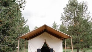 A tent with a wooden deck and two chairs. - Yellowstone Family Safari Tent, sleeps 7 w/ 1 king (Island Park)
