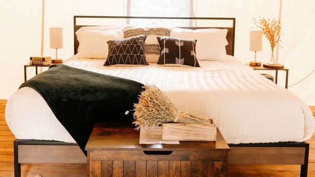 A tent-style bedroom with a bed, pillows, a bedside table, and a lamp. - Yellowstone Family Safari Tent, sleeps 7 w/ 1 king (Island Park)