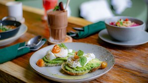 Ett matbord med en tallrik avokadotoast, en skål med sallad och en rosa drink.