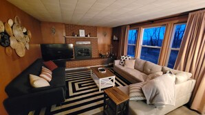 A living room with a fireplace, a black sofa, a beige sofa, a coffee table, and a TV. - Woodland cabin on the Bay (Peshtigo)