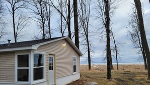 A small, single-story house with a gabled roof, a front door, and a window on the left side. - Woodland cabin on the Bay (Peshtigo)