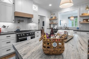 A modern kitchen with white cabinetry, a herringbone-patterned backsplash, a gas stove, and a wicker basket with food items on the island.