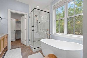 A modern bathroom with a glass-enclosed shower, a freestanding bathtub, and a large window offering a view of trees. - New luxury build w/ Hot tub - Immaculate Vita Huset in Sister Bay (Sister Bay)