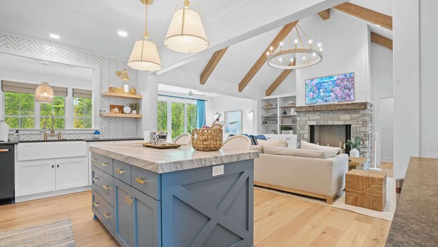 A modern kitchen with a central island, pendant lighting, and a stone fireplace.