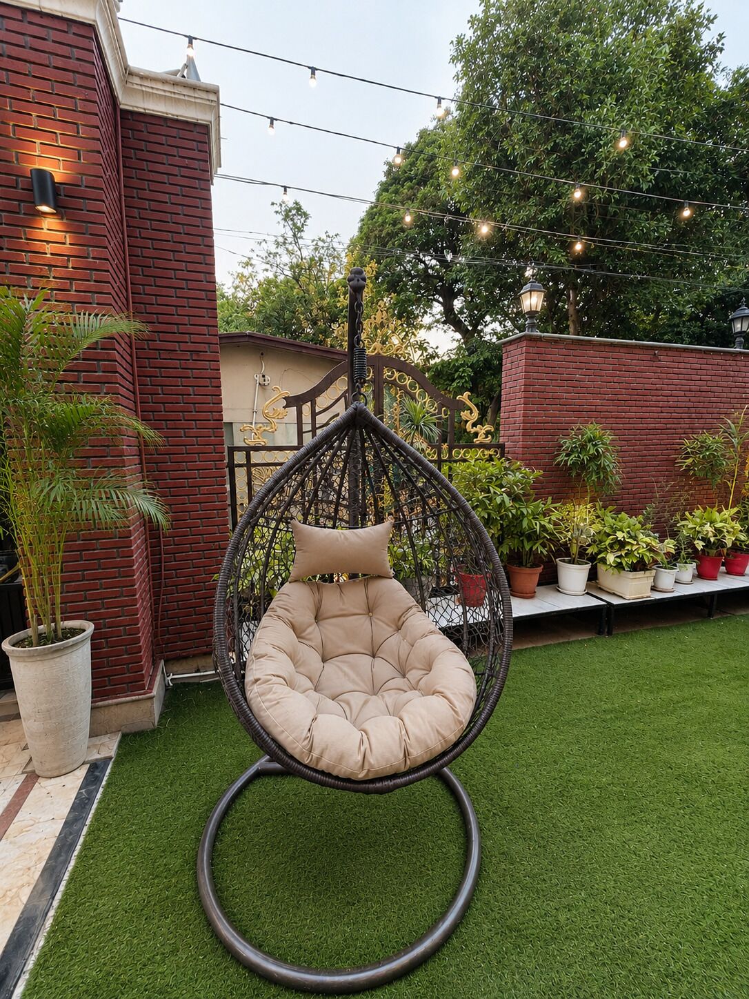 Une chaise suspendue avec un coussin, un mur de briques et des plantes en pot, le tout dans un décor de jardin.
