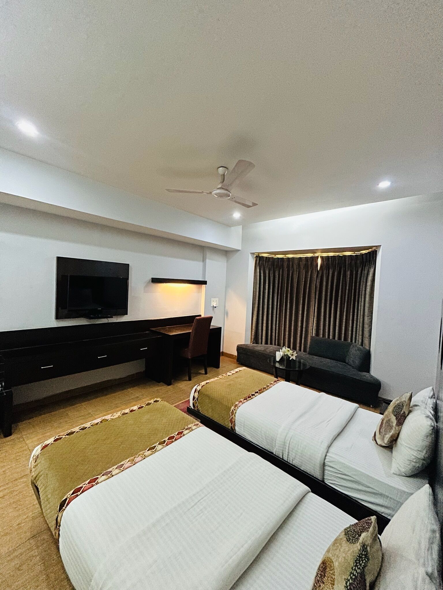 A hotel room with two beds, a desk, a chair, a television, and a window with curtains.