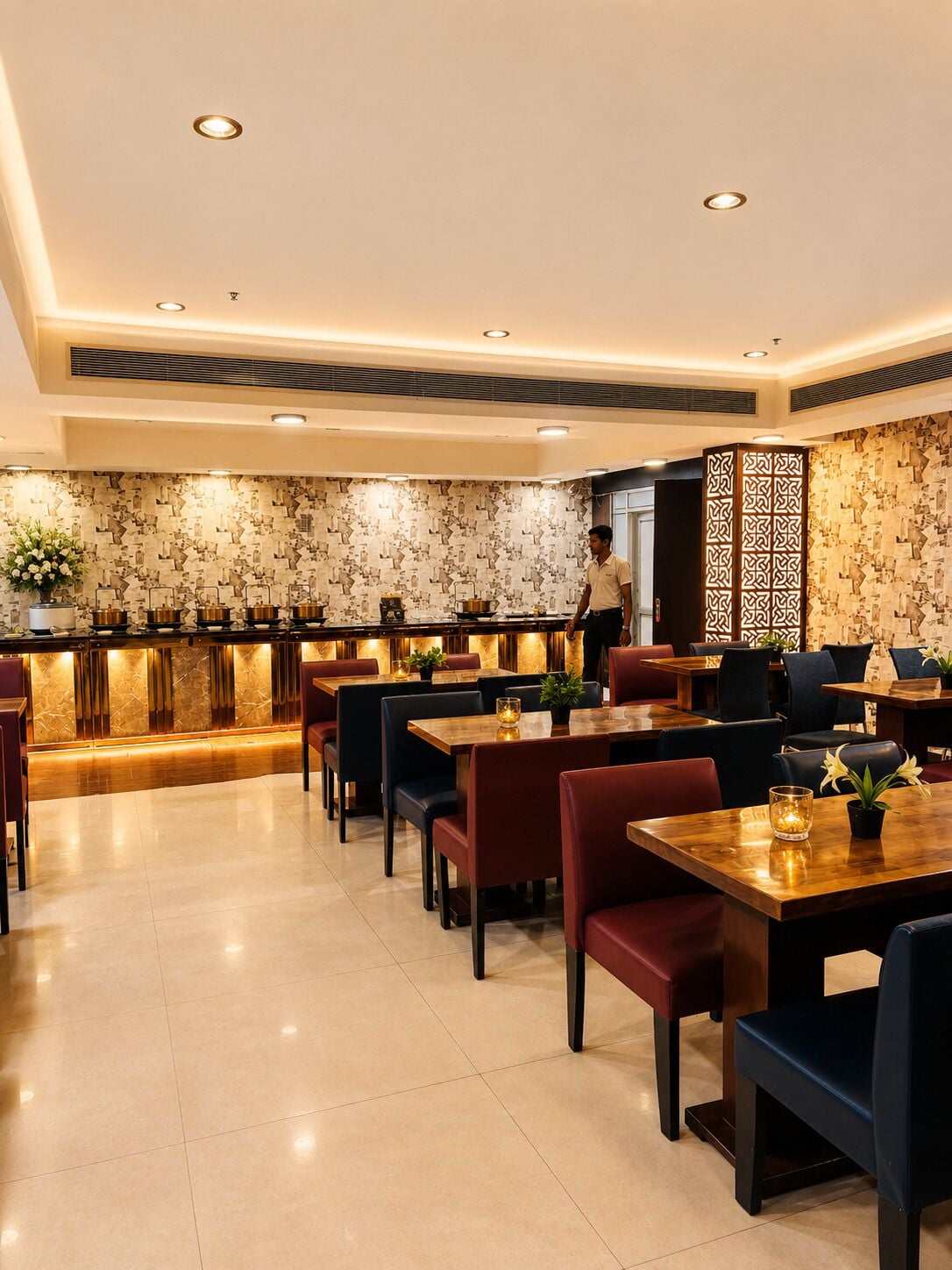 A restaurant with a modern interior, featuring a central bar area, multiple dining tables, and a patterned wall.