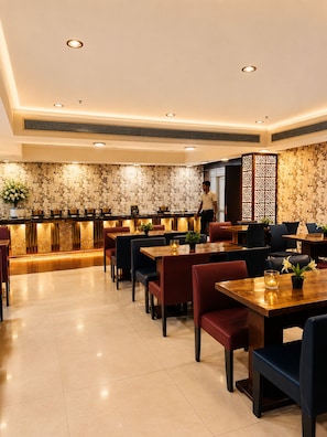 A restaurant with a modern interior, featuring a central bar area, multiple dining tables, and a patterned wall. - Hotel Cymbal-sector 31 Gurgaon (Gurugram)