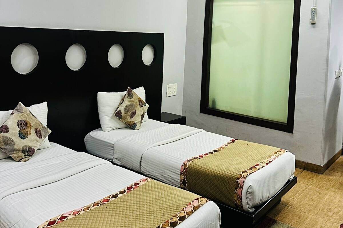 Habitación de hotel con dos camas, ventilador de techo, ventana con persianas y un cuadro pequeño en la pared.