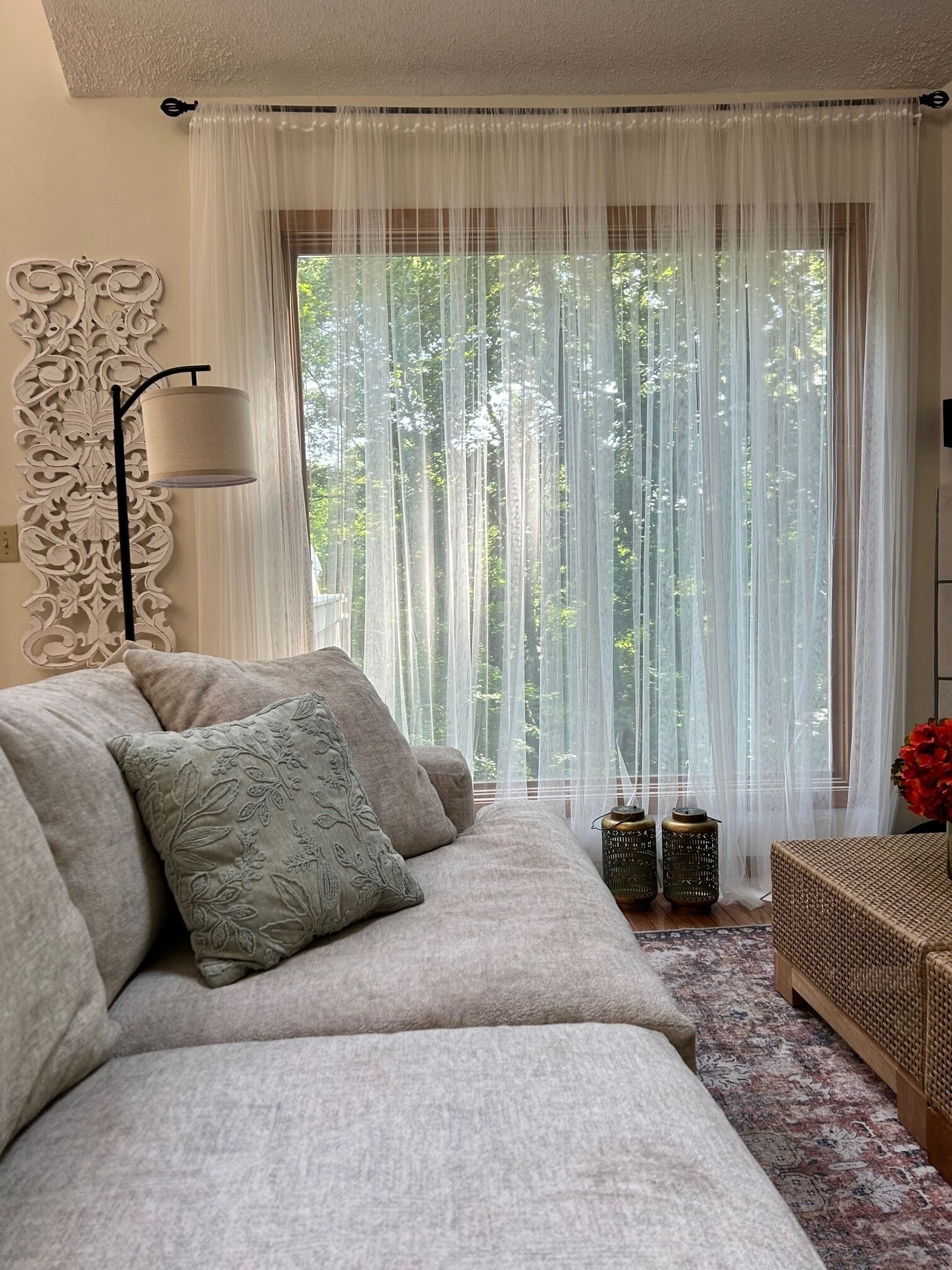 Een gezellige woonkamer met een bank, decoratieve kussens, een vloerlamp en uitzicht door dunne gordijnen.