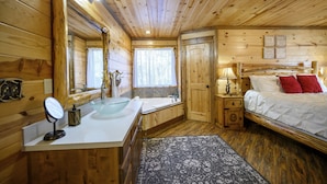 Dormitorio de cabaña de madera con cama, mesita de noche, lámpara y un espejo grande.