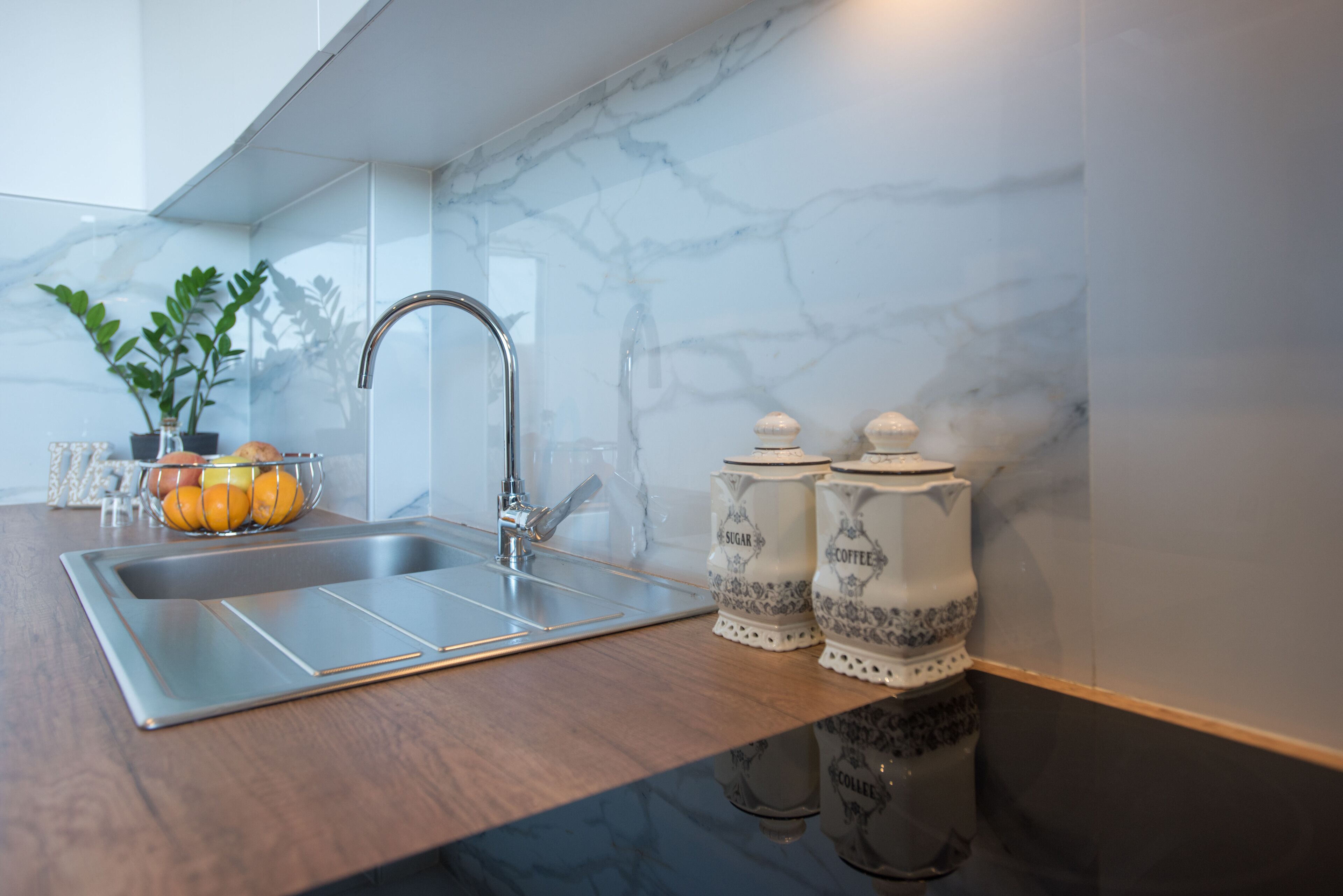 A kitchen with a marble backsplash, a stainless steel sink, and two sugar and coffee containers.