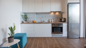 Une cuisine moderne avec des armoires blanches, un pare-feu en marbre, un four encastré et un réfrigérateur en acier inoxydable.