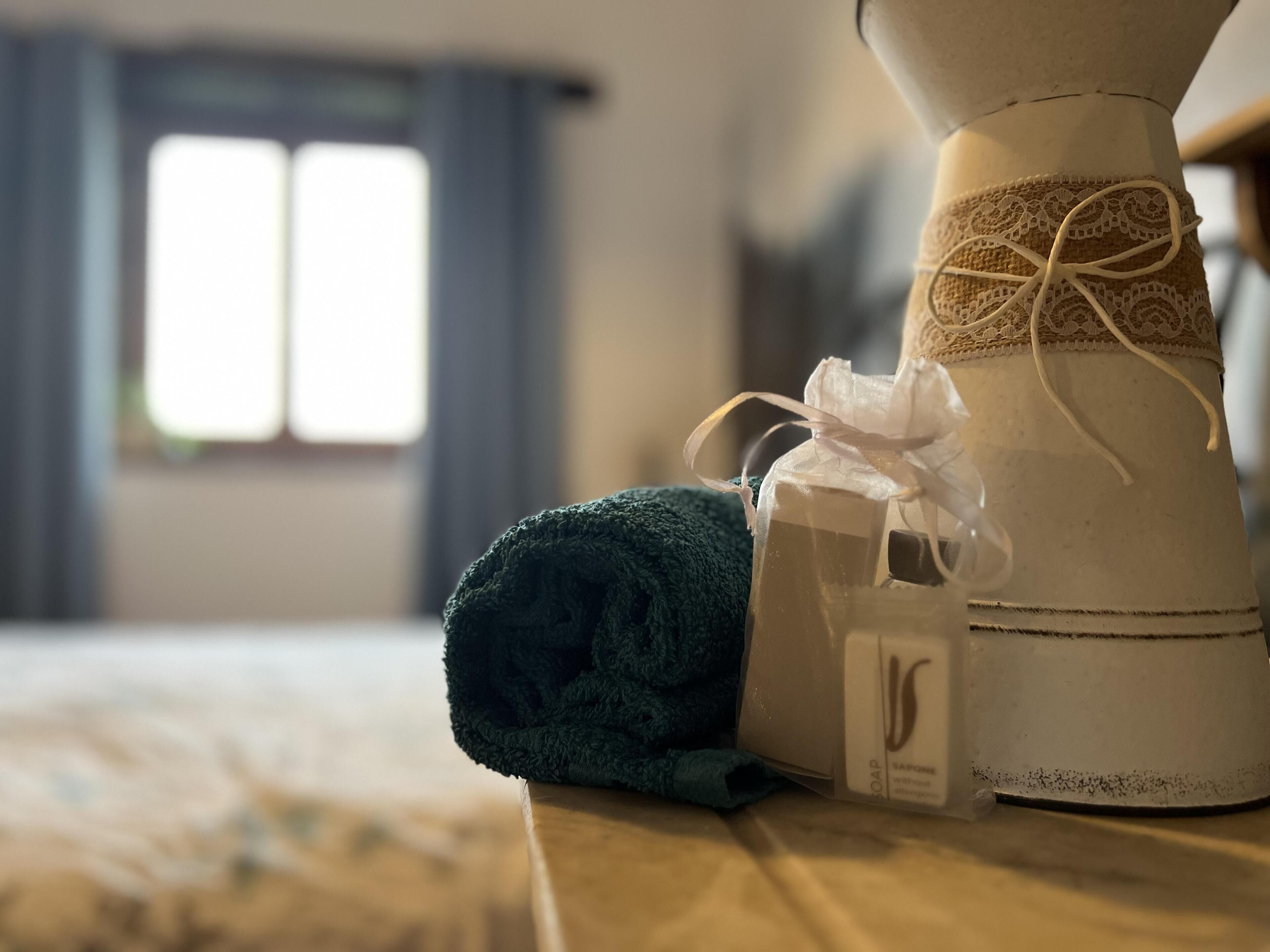 A neatly made bed with a rolled-up towel and a white bottle of soap.