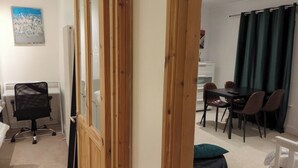 Een kamer met een bureau, stoel, eettafel met stoelen en een raam met gordijnen.