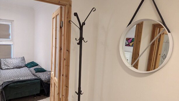 Een slaapkamer met een bed, een kapstok en een ronde spiegel aan de muur.