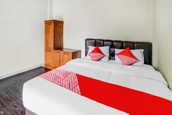 Una cama bien hecha con una colcha blanca y roja, dos almohadas rojas y una mesita de noche de madera.