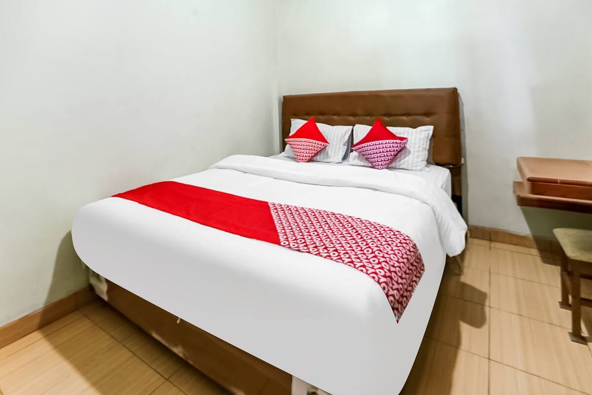 Una cama bien hecha con un edredón rojo y blanco, dos almohadas y un cabecero de madera.