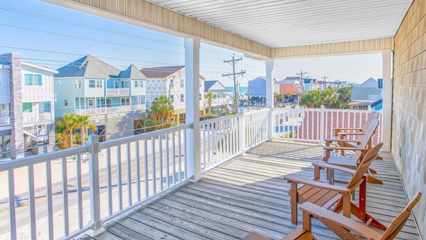 A wooden deck with chairs and tables, overlooking a street with colorful buildings. - 5bed/5bath house with heated pool and fire pit! (Murrells Inlet)