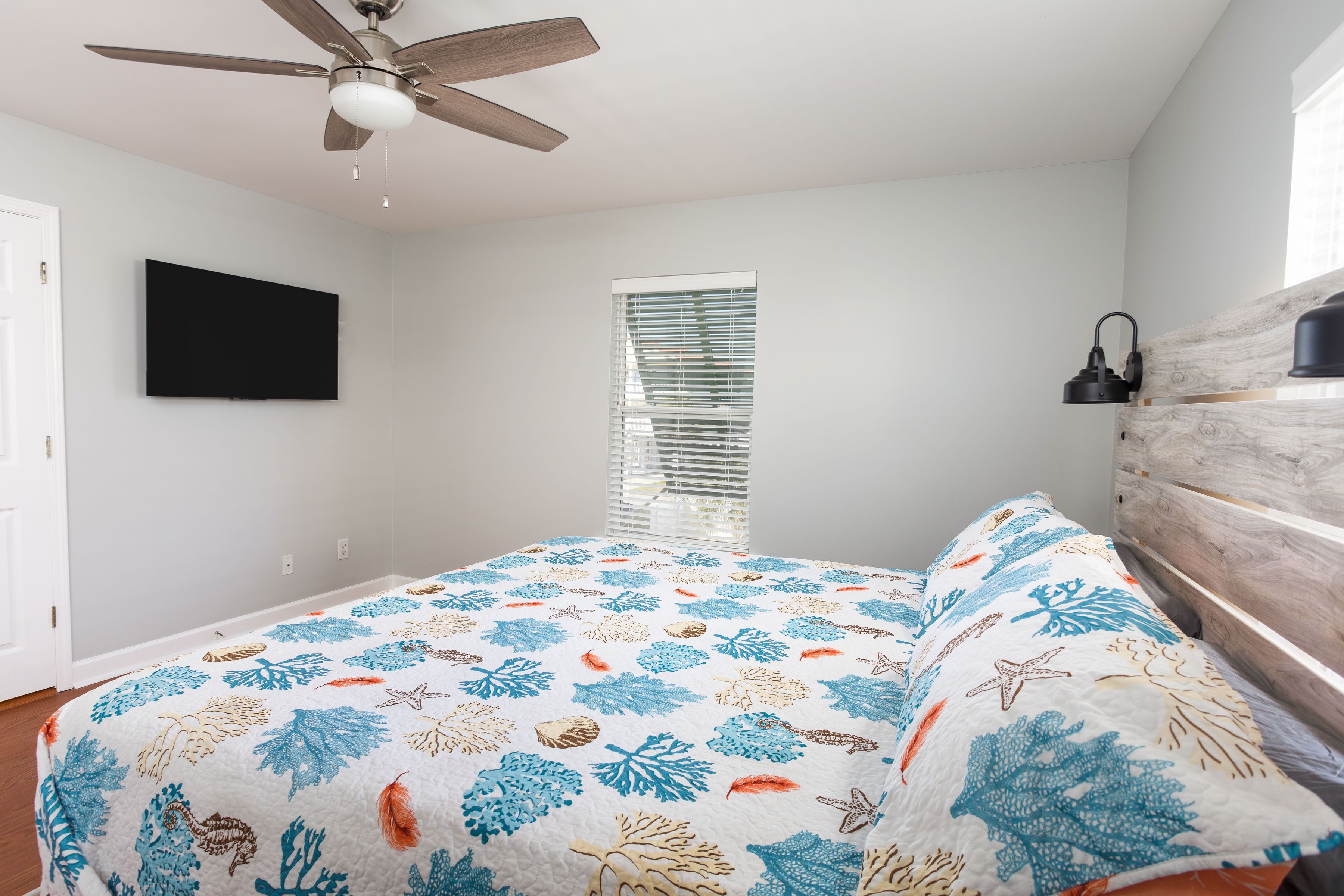 A bedroom with a bed, a ceiling fan, a TV, and a window with blinds.