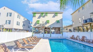 A swimming pool area with lounge chairs and a building with multiple windows and air conditioning units. - 5bed/5bath house with heated pool and fire pit! (Murrells Inlet)