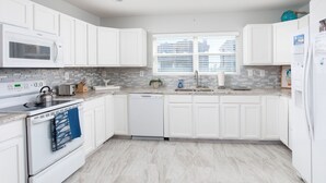 A modern kitchen with white cabinetry, a built-in microwave, a dishwasher, and a window with blinds. - 5bed/5bath house with heated pool and fire pit! (Murrells Inlet)