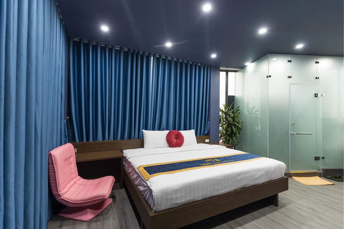 A modern hotel room with a bed, a pink chair, and a large window.