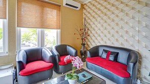 A room with two black leather sofas with red cushions, a white vase with flowers, and a patterned wall.