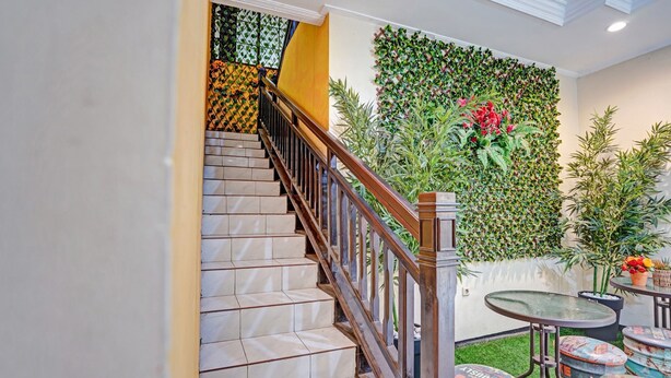 A staircase with a wooden railing, a green wall with plants, and a small round table with stools.