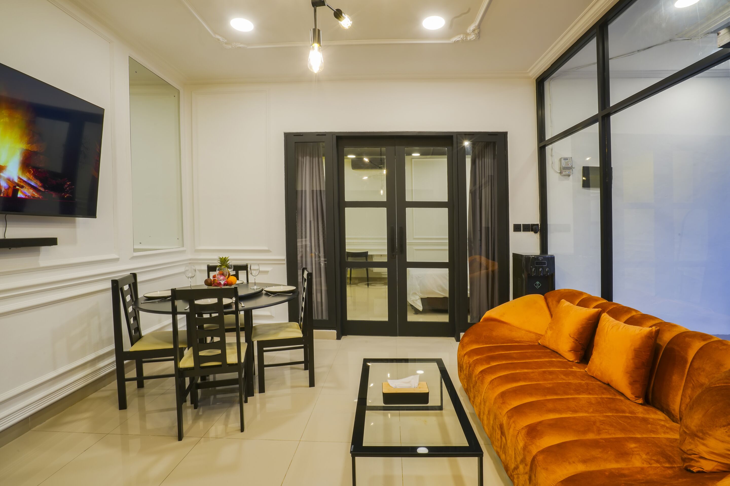 Ein Wohnzimmer mit einer Couch, einem Esstisch mit Stühlen, einem an der Wand montierten Fernseher und einer Glastür zu einem Balkon.