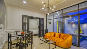 A modern living room with a glass coffee table, a sofa, and a dining area with chairs and a table set for two. - Villa Canberra (Seminyak)