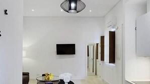 Een moderne eetruimte met een tafel voor vier personen, een witte vaas als middelpunt en een flatscreen televisie aan de muur.