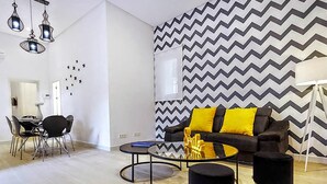 Een moderne woonkamer met een zwart-geel kleurenschema, een ronde salontafel en twee zwarte voetenbankjes met gouden poten.