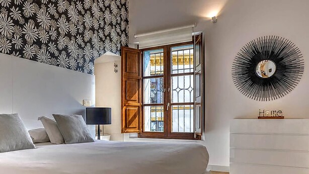Een slaapkamer met een bed, nachtkastje, dressoir, raam met uitzicht en een decoratieve spiegel.