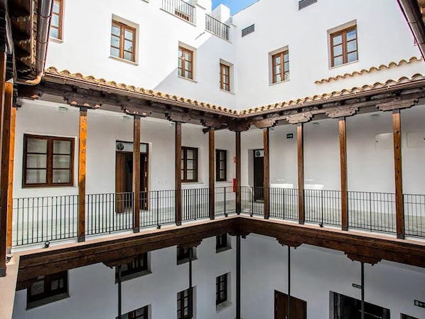 A courtyard with white walls and wooden beams, featuring multiple doors and windows.
