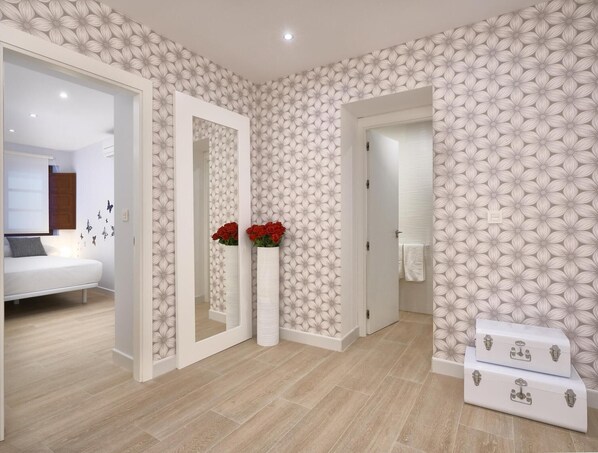 A modern bedroom with a bed, a mirror, a vase with flowers, and a suitcase. - PALACIO BUENAVISTA LUXURY APARTMENTS B.3 (Sevilla)