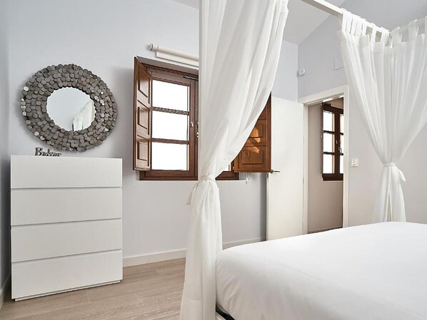 Une chambre à coucher avec un lit, une commode, un miroir et une fenêtre avec des rideaux.