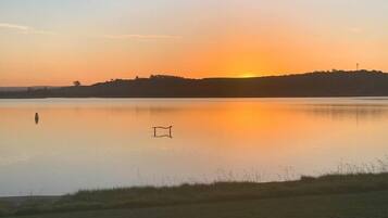 Relax on the serene lakeside bench, surrounded by a peaceful grassy area and distant hills.