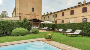 Una piscina con una torre de ladrillo, sillas de descanso y un jardín.