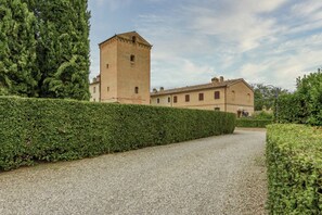 Un edificio con una torre, un sendero de grava y un seto.