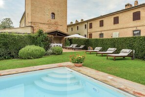 Una piscina con una torre de ladrillo, sillas de descanso y un jardín.