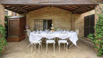 A covered outdoor dining area with a brick wall, a wooden door, and a table set for four.